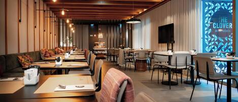 Um restaurante moderno com vigas de madeira, iluminação pendente e diversos tipos de assentos, incluindo mesas e cadeiras.
