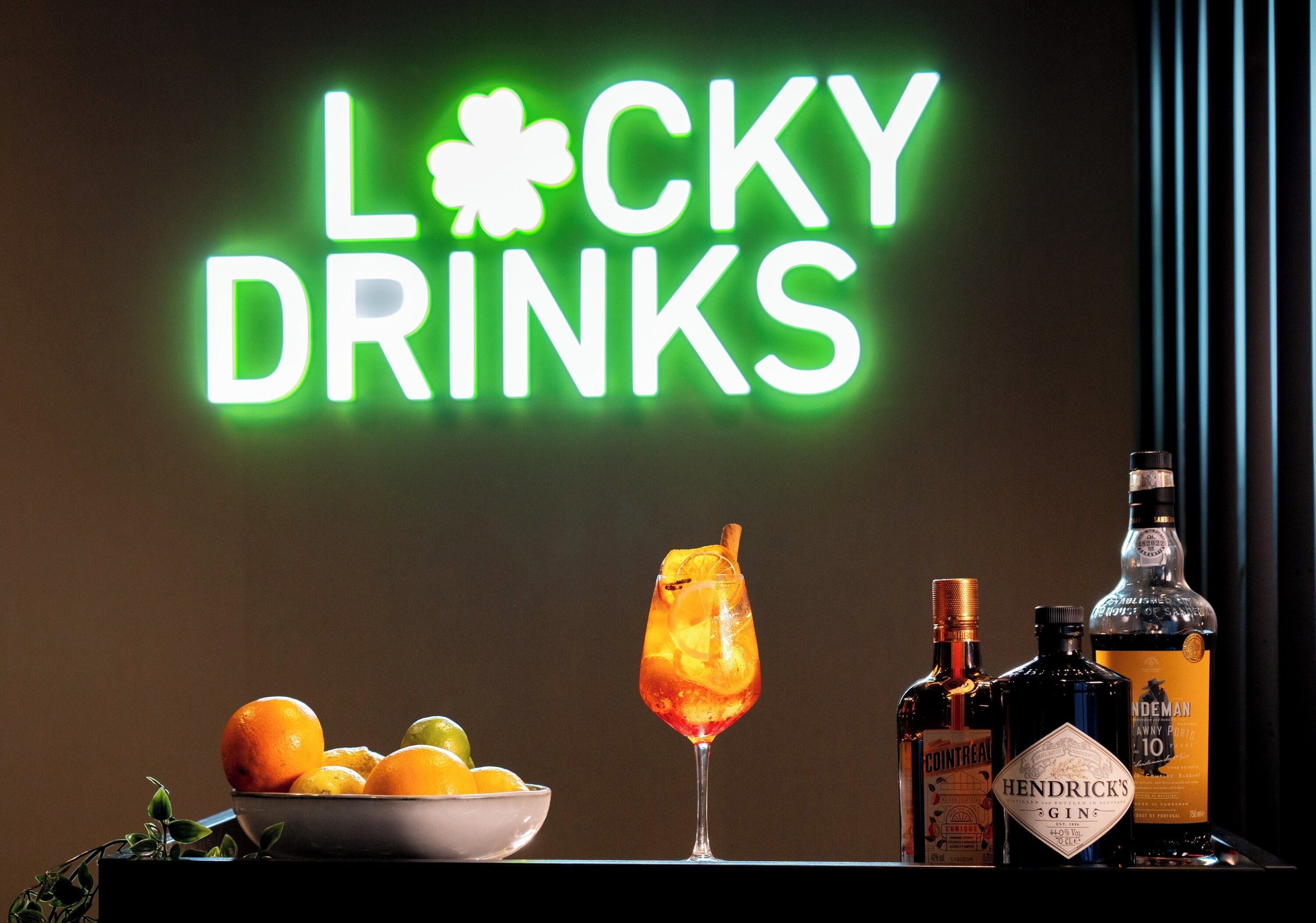 A neon sign reading "Lucky Drinks" with a cocktail glass and bottles of Hendrick's Gin and Cointreau on a table.