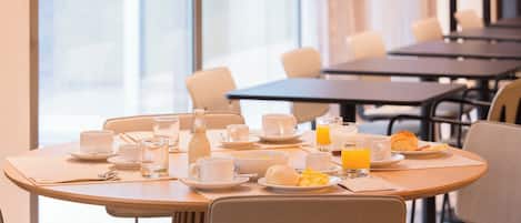 Un ambiente para desayunar con mesas, sillas y vistas de la ciudad a través de grandes ventanales.