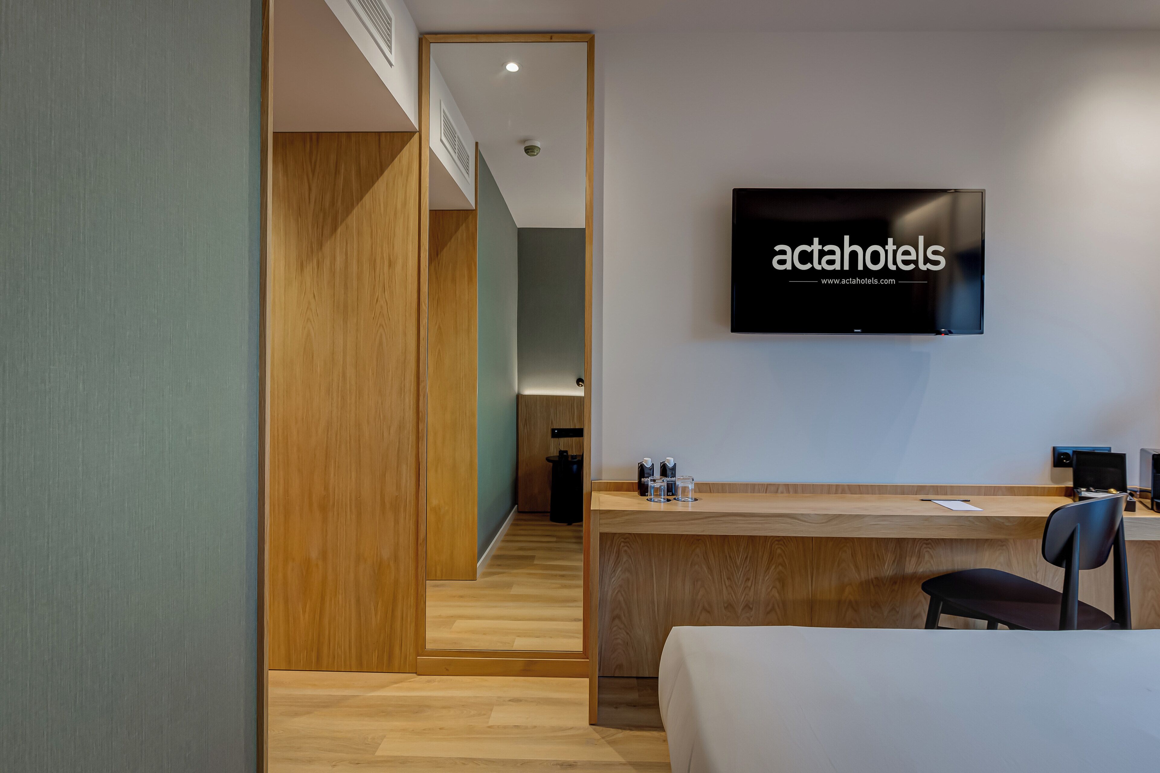 A hotel reception area with a wooden desk, a television mounted on the wall, and a staircase leading to the upper floor.