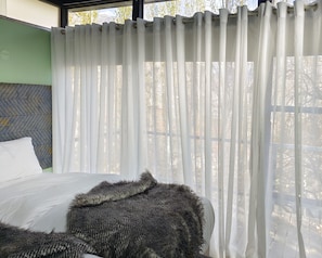 Un dormitorio con una cama, un almohadón blanco y una manta gris.