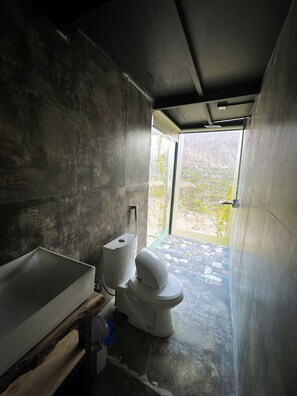 A modern bathroom with a large bathtub, toilet, and a window providing a view of the outdoors. - Stunning Cliff-edge 2-bedroom Chalet in Karimabad (Karimabad)