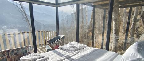 A bedroom with a large window overlooking a mountainous landscape.