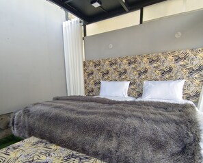 Ein Bett mit einem gemusterten Kopfteil, weißen Kissen und einer flauschigen, grauen Decke.