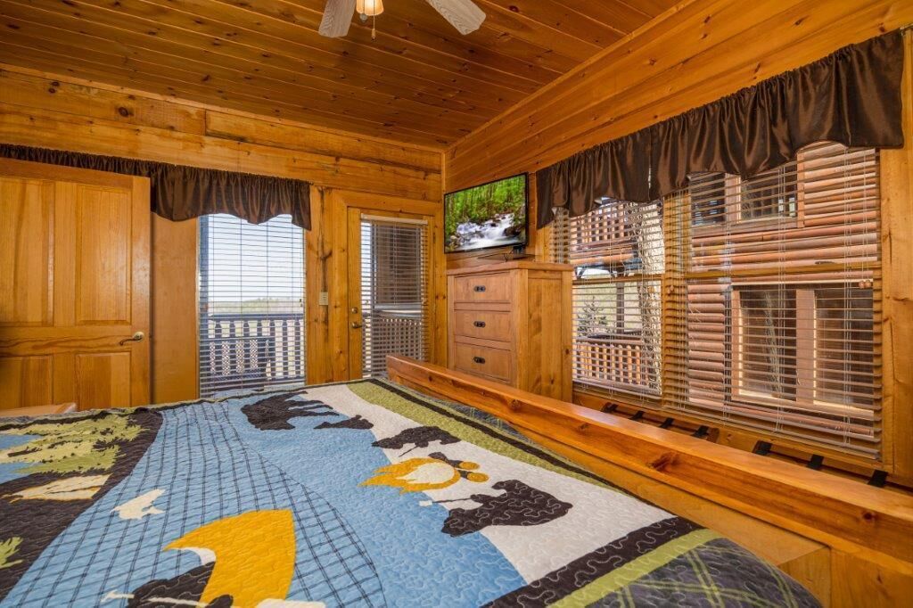 Ein Zimmer einer Holzhütte mit einem Bett, einem Fernseher und einem Fenster mit Jalousien.