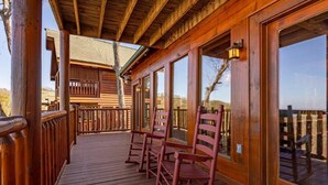 A wooden deck with rocking chairs and large windows.
