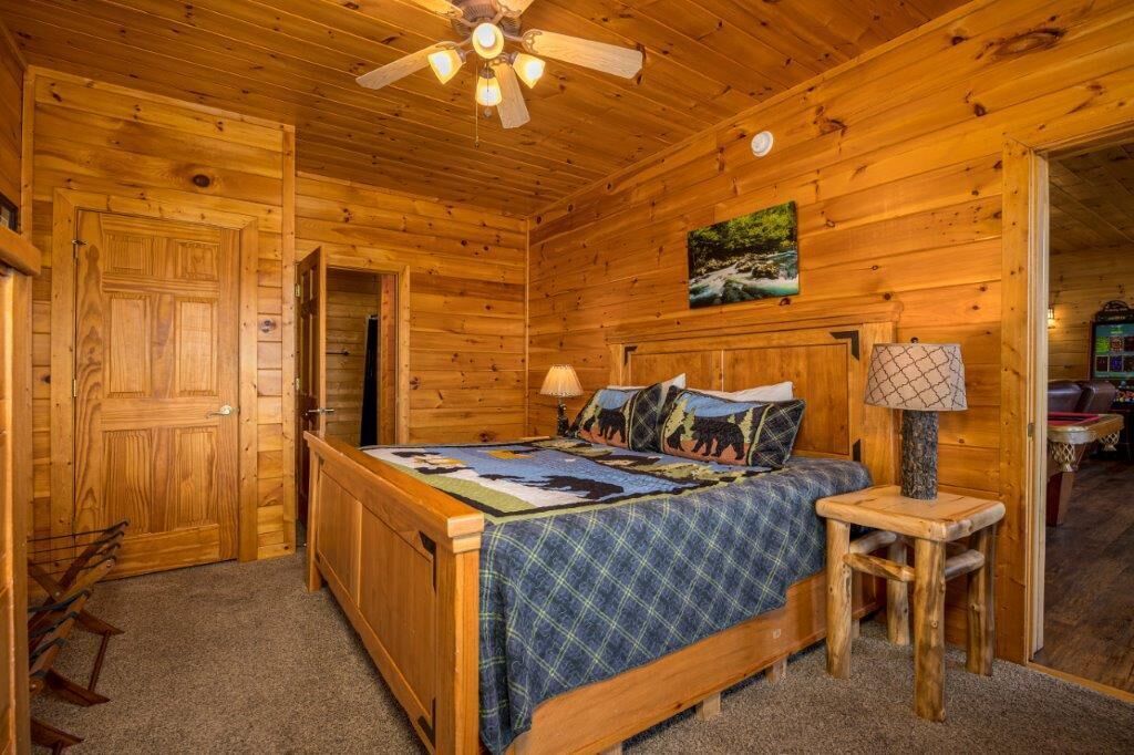 Un dormitorio de cabaña de madera con una cama, una mesita de noche, una lámpara y un ventilador de techo.