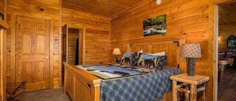 Un dormitorio de cabaña de madera con una cama, una mesita de noche, una lámpara y un ventilador de techo.