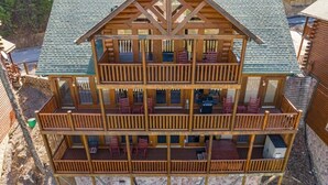 A multi-story log cabin with a balcony on each floor, outdoor seating, and a fireplace.