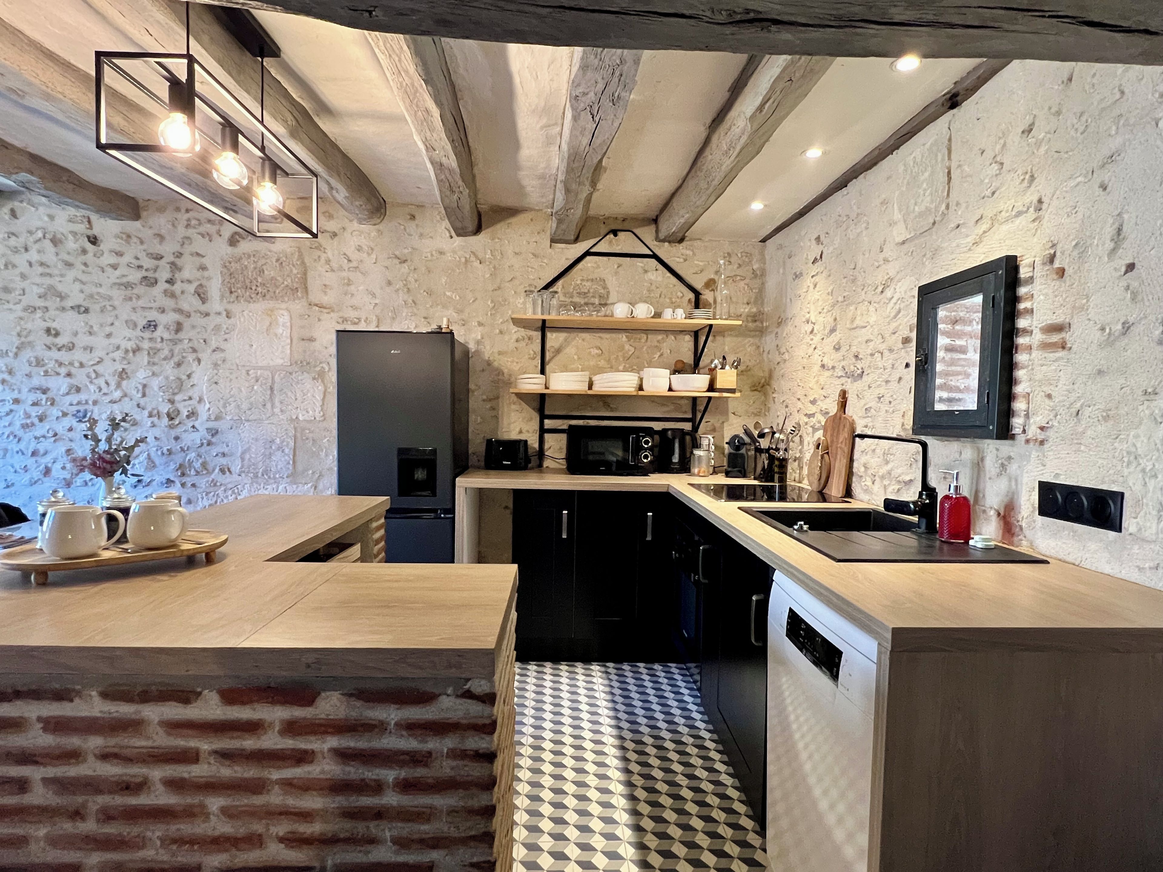 A kitchen with a brick wall, wooden beams, a black refrigerator, a microwave, and a sink.