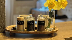 A wooden tray with three glass jars labeled 'FILTRE A THE,' 'The Verve,' and 'CHOCOLAT,' and a glass vase with yellow flowers. - Le Cottage des Chalands (Saint-Georges-sur-Cher)