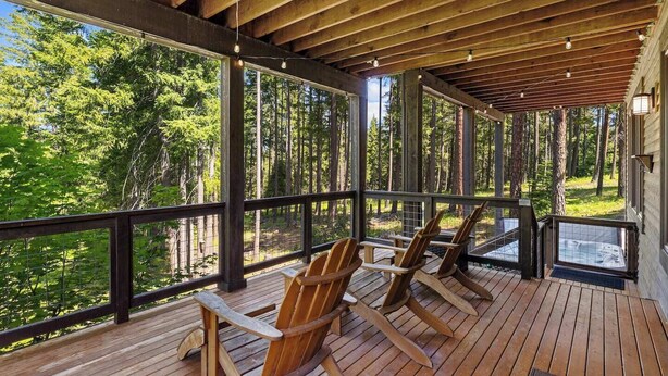 Een houten terras met Adirondack-stoelen met uitzicht op een bebost gebied.