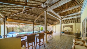 A covered outdoor area with a pool, wooden furniture, and patterned flooring. - Villa Matahari (Gili Meno)