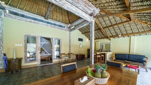 A spacious room with a wooden dining table, a sofa, and a large mirror. - Villa Matahari (Gili Meno)