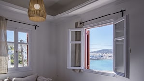 Ein Zimmer mit einem Bett, einem Schlafsofa, einem Fenster mit Blick auf eine Küstenstadt und einer Pendelleuchte.