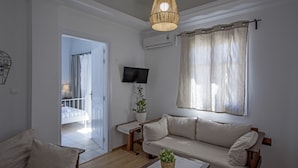 Ein Wohnzimmer mit einer Couch, einem Fernseher, einer Pflanze und einem Fenster mit Vorhängen.