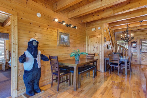 A wooden cabin interior with a dining table, chairs, a bear mascot, and a chandelier. - Royal Vista Lodge (Sevierville)