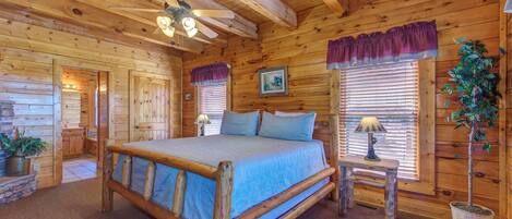 Dormitorio de cabaña de troncos con una cama de madera, un ventilador de techo, una ventana con persianas y una planta en maceta.