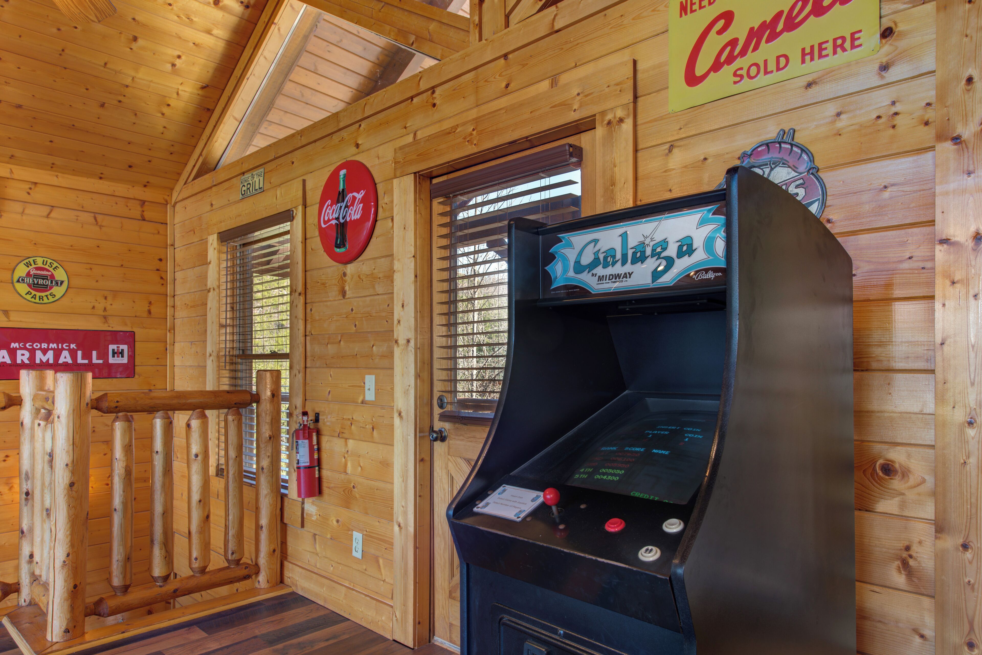 A wooden interior with a Coca-Cola sign, a Galaxie arcade machine, and a sign for McCormick Farmall.