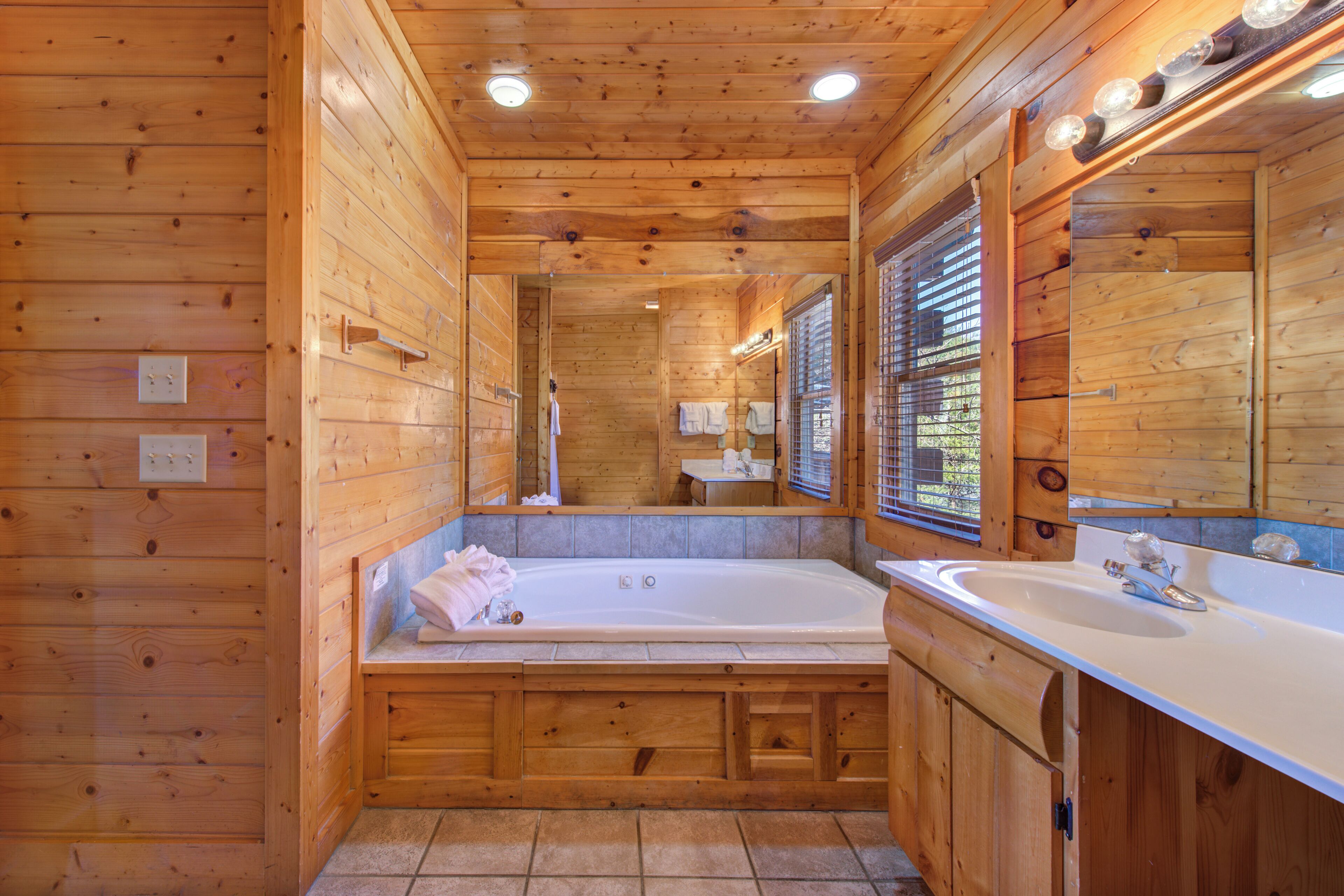A wooden cabin bathroom with a bathtub, sink, and large mirror.