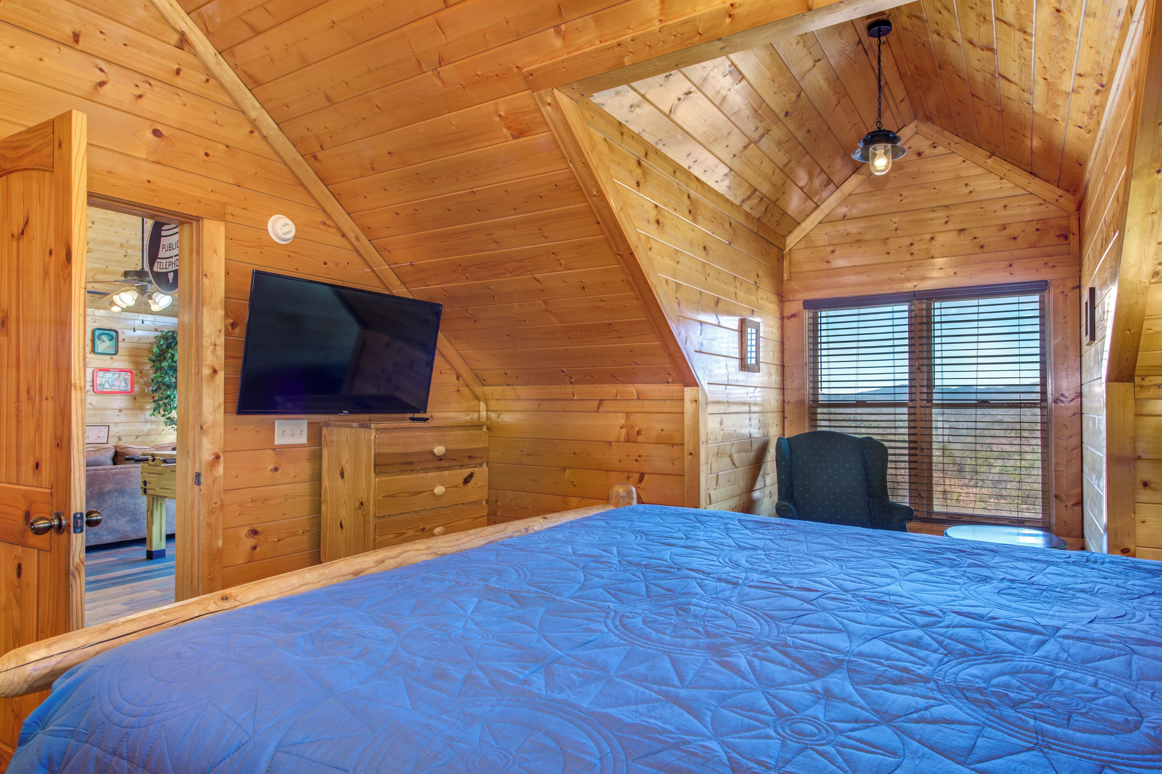 Une chambre dans une cabane en bois, avec un lit, un téléviseur fixé au mur et une fenêtre avec des stores.