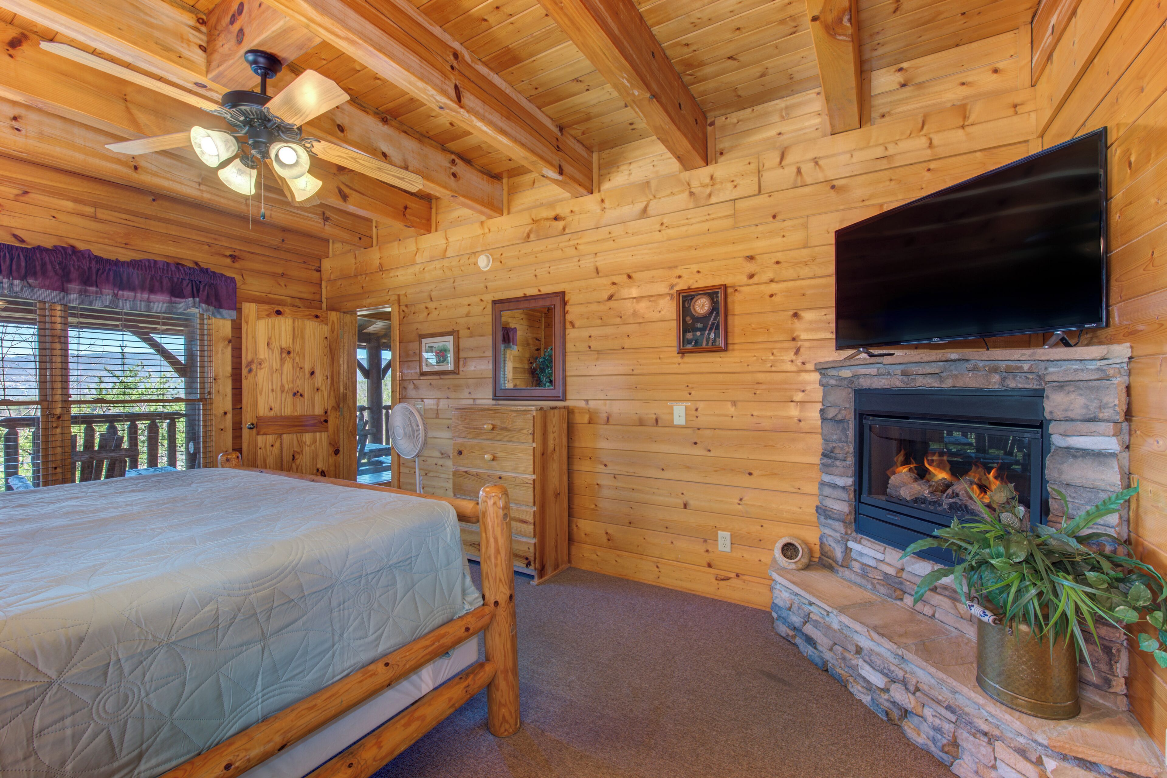 A wooden cabin interior with a bed, a fireplace, a television, and a ceiling fan.