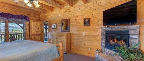A wooden cabin interior with a bed, a fireplace, a television, and a ceiling fan.