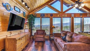 A spacious room with wooden walls, a large TV, a leather couch, and a ceiling fan. - Royal Vista Lodge (Sevierville)