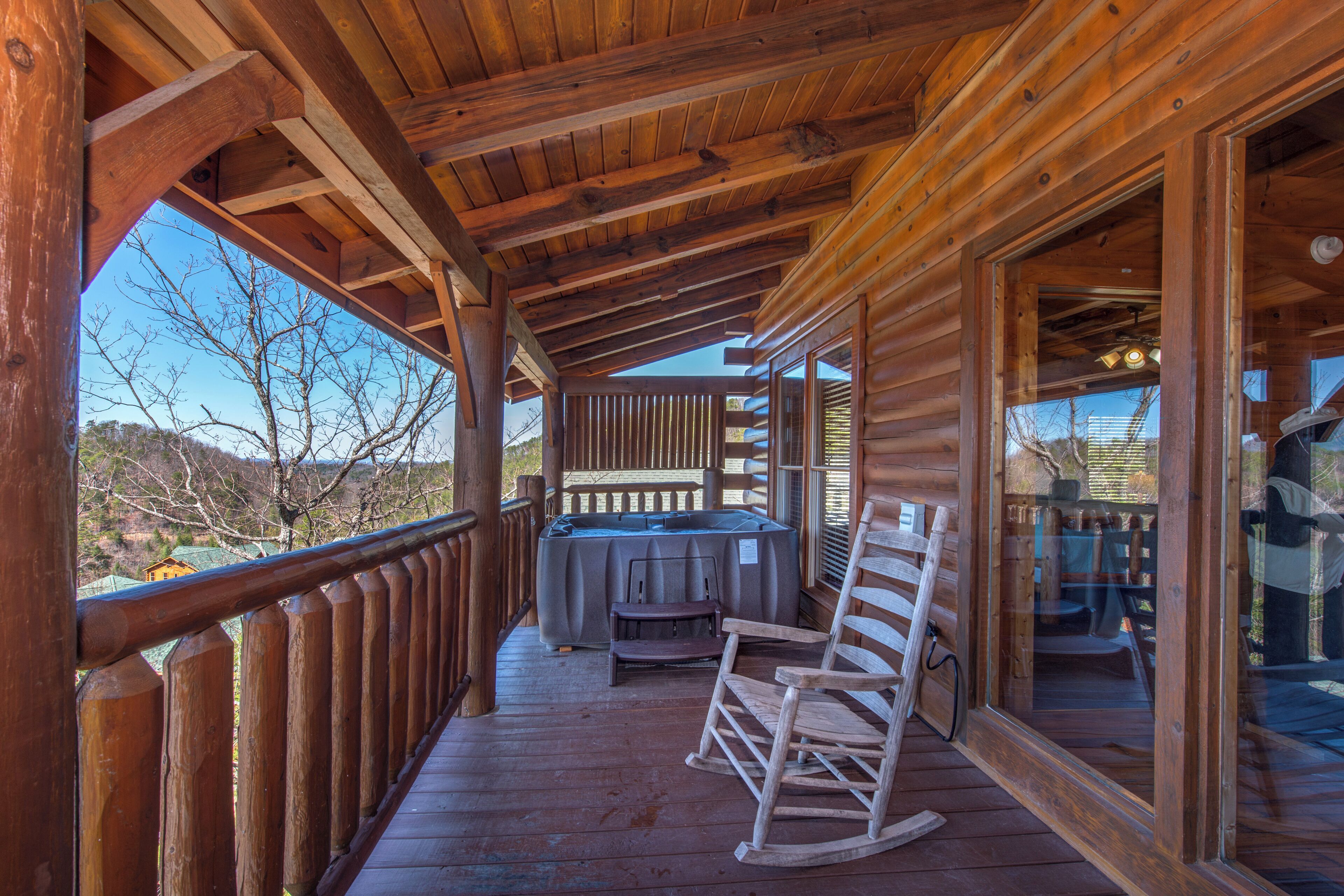 A wooden deck with a hot tub, rocking chairs, and a table.