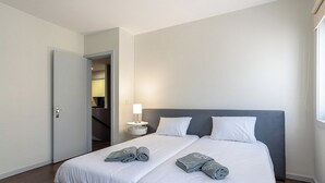 A modern hotel room with a large bed, two pillows, a bedside table with a lamp, and a door leading to a bathroom. - Porto Gaia City House (Vila Nova de Gaia)