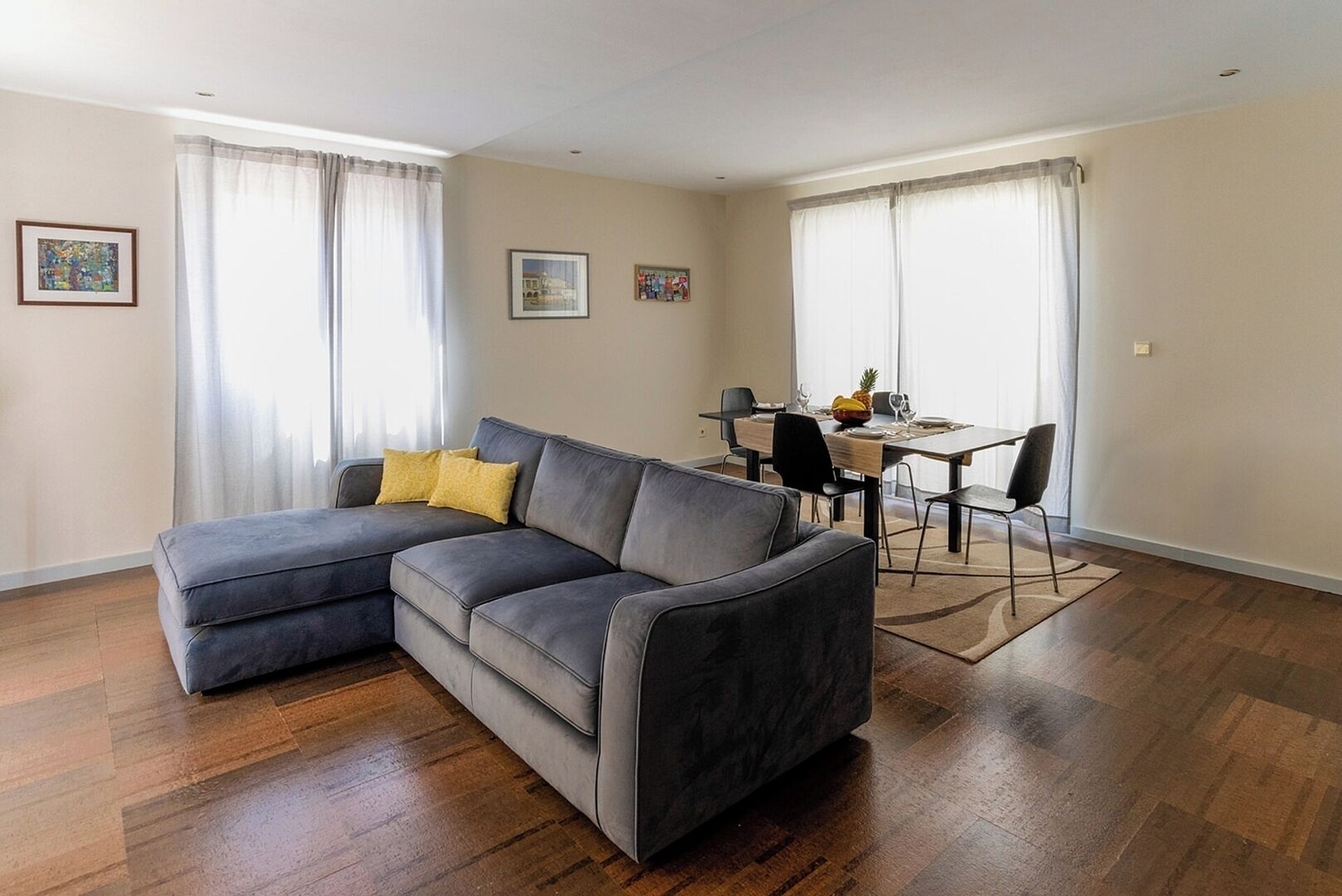 Ein modernes Wohnzimmer mit einem grauen Ecksofa, einem Esstisch mit Stühlen und Holzboden.