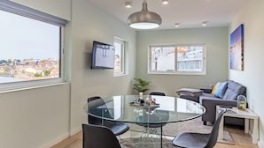 A modern living room with a glass dining table, grey sofa, and a TV mounted on the wall. - Lu | Localização Central, Vista Rio and Nespresso (Vila Nova de Gaia)