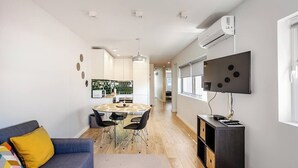 A modern living space with a sofa, a dining table with chairs, a TV mounted on the wall, and an air conditioning unit. - Lu | Localização Central, Vista Rio and Nespresso (Vila Nova de Gaia)