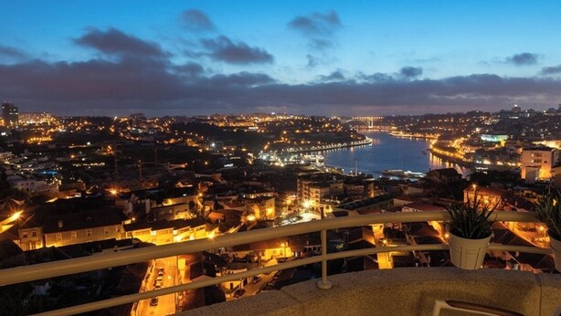 A balcony with a view of a cityscape at dusk, featuring a table and chairs, and a potted plant. - Porto Gaia River View (Vila Nova de Gaia)