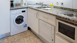 A compact kitchen with white cabinets, a built-in washing machine, a sink, and a stove. - Porto Gaia River View (Vila Nova de Gaia)