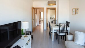 A modern living room with a TV, a dining area with a table and chairs, and a kitchen in the background. - Porto Gaia River View (Vila Nova de Gaia)