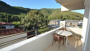 Een balkon met een tafel en stoelen, met uitzicht op een heuvel waarop gebouwen en bomen staan.