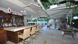 Een bar met een toonbank, stoelen, en een zitgedeelte aan het zwembad met tafels en stoelen.