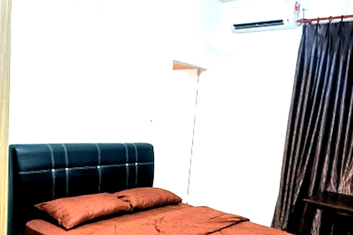 A bed with a dark headboard and a brown bedspread in a room with a wooden floor and a white ceiling.