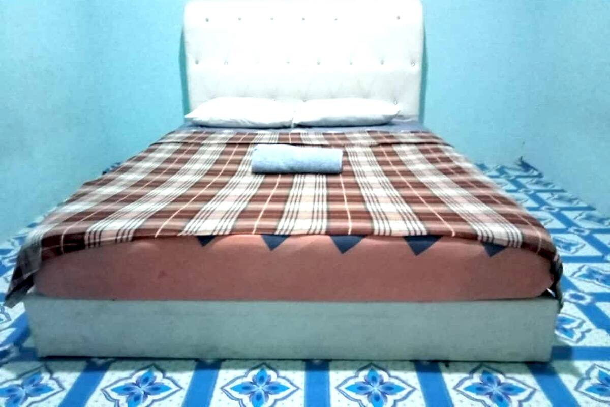 A bed with a plaid bedspread and a pillow, set against a blue wall with a patterned floor.