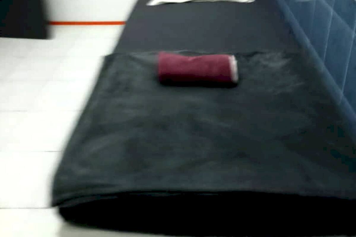 A narrow room with a bed against the wall, a white pillow, and a red object on the bed.