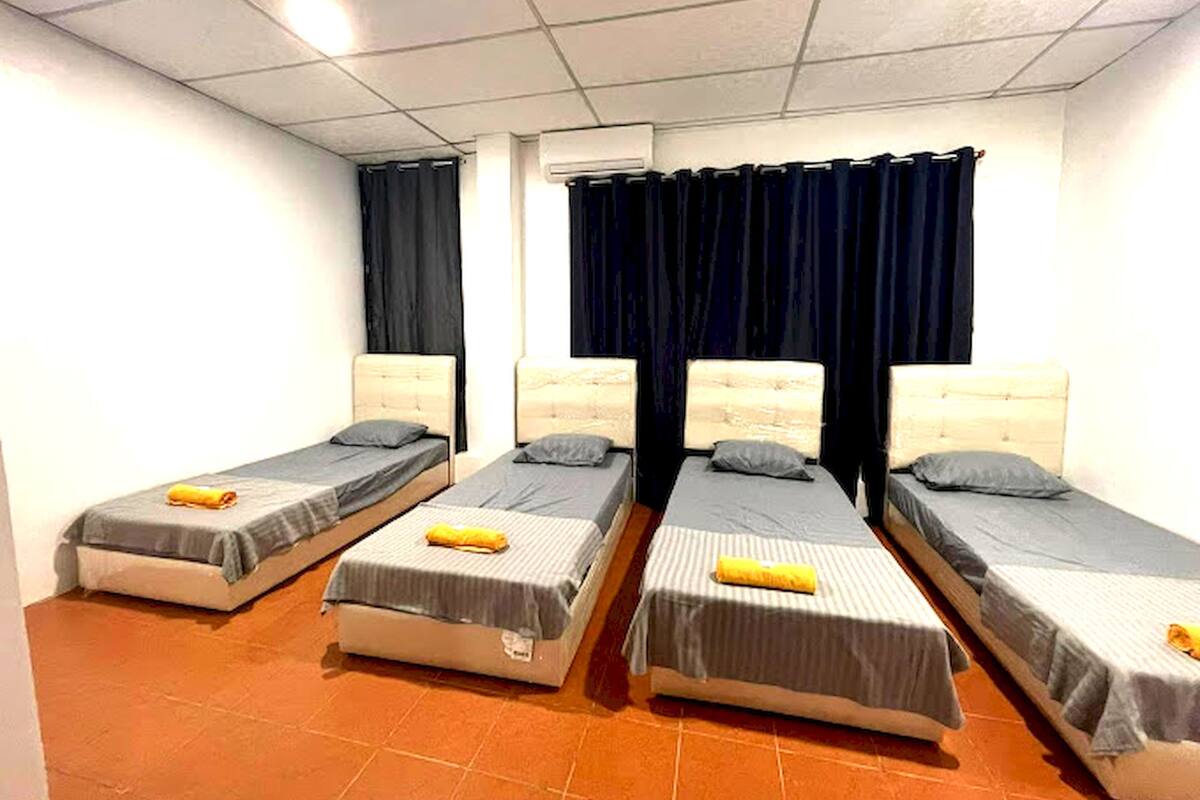 A room with four single beds arranged in a row, each with a pillow and a rolled towel.