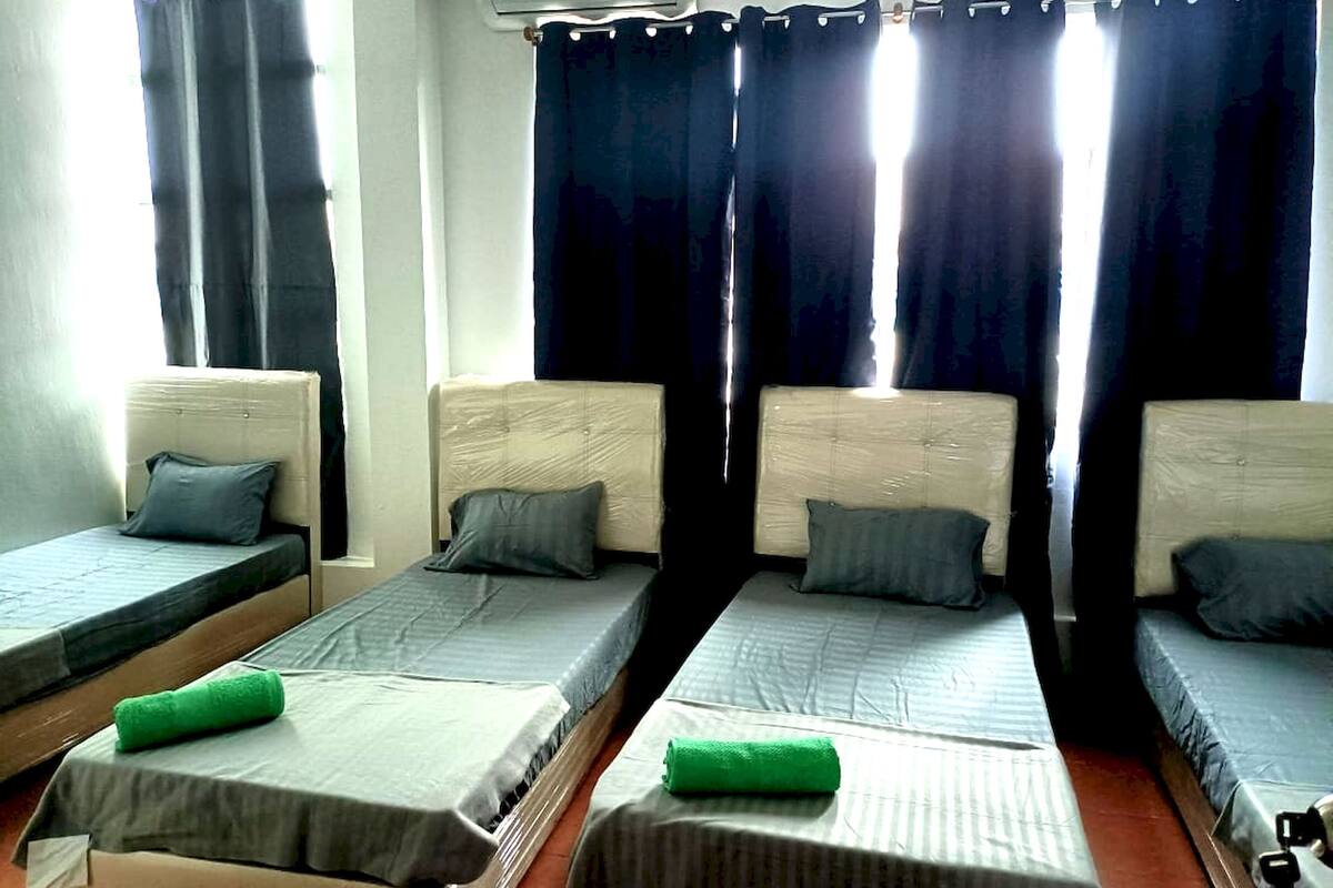 A room with four single beds, each with a pillow and a green towel.