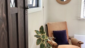 Une pièce avec une porte en bois, une plante en pot, une chaise en bois avec un coussin et un miroir rond accroché au mur.