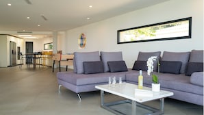 Een moderne woonkamer met een grijze bank, een witte salontafel en een eethoek op de achtergrond.