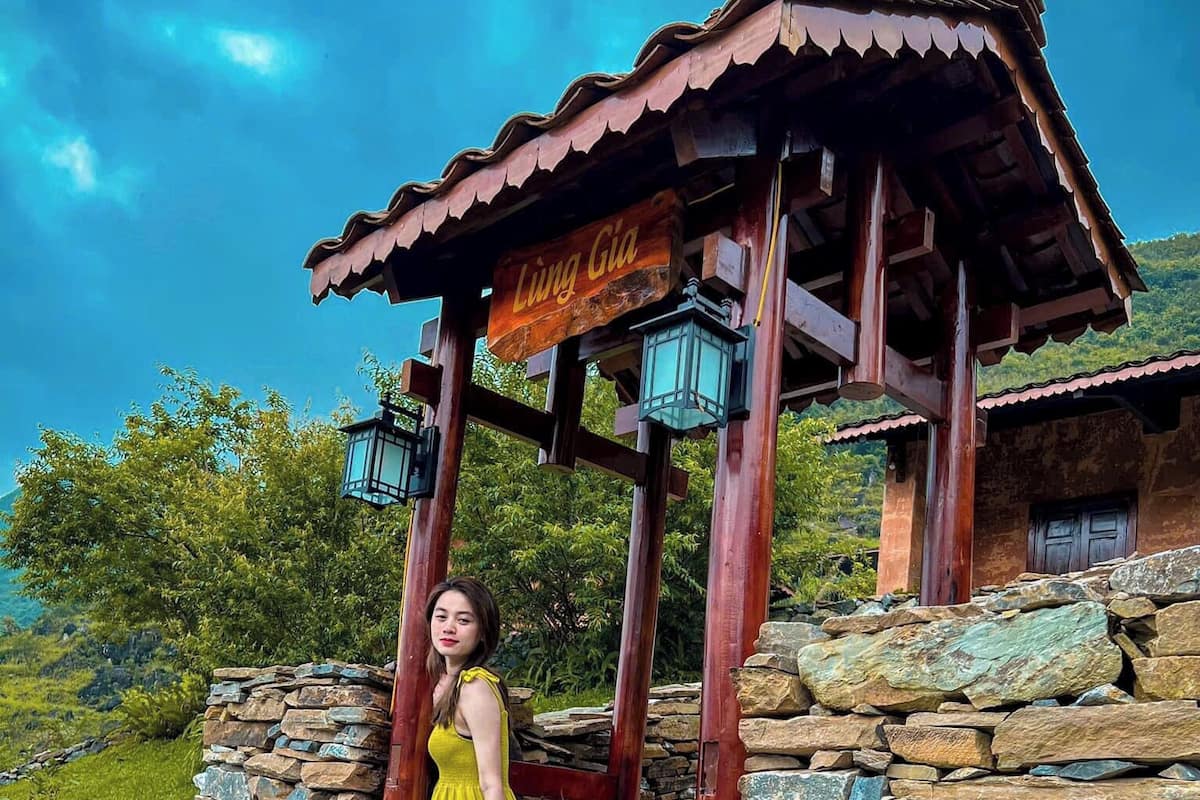 A woman in a yellow dress standing at the entrance of a rustic stone building with a wooden structure above.