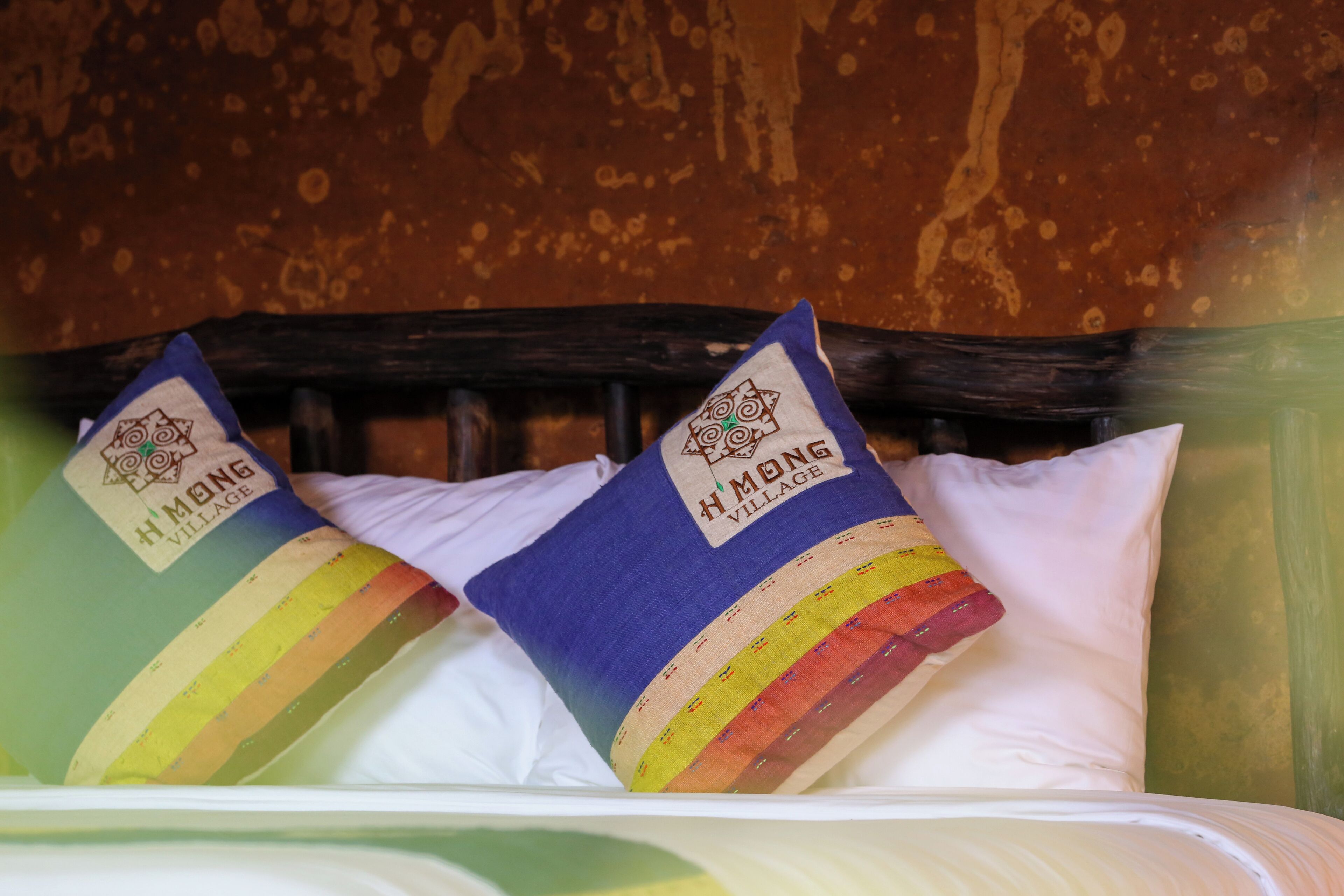 A bed with two pillows, each featuring a colorful design and the text "Hmong Village".