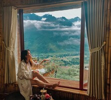 Uma pessoa sentada perto de uma janela com vista para montanhas e vegetação.
