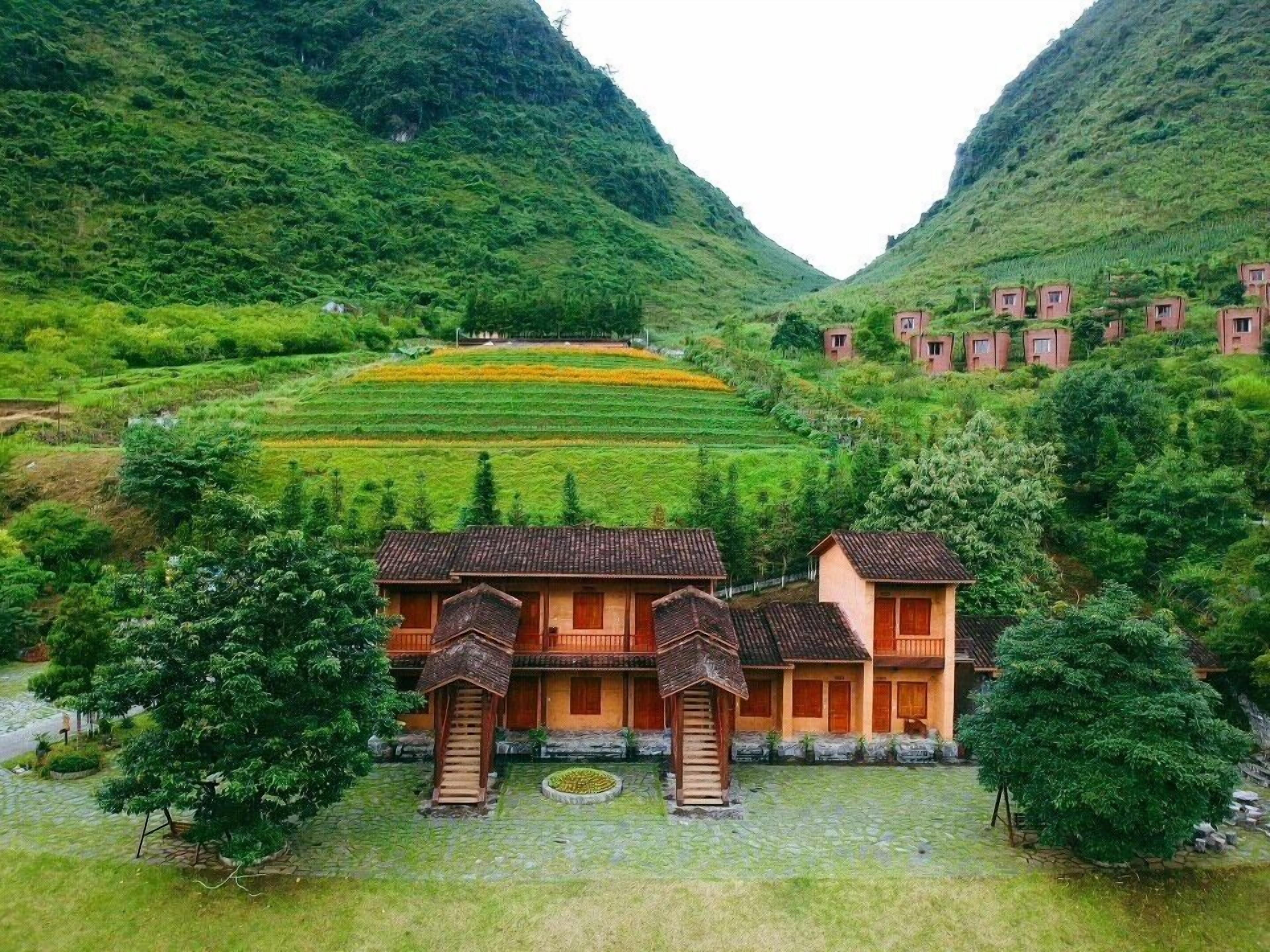 A traditional building with a tiled roof and wooden balconies, surrounded by lush greenery and terraced fields.