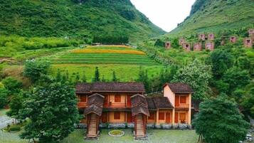A traditional building with a tiled roof and wooden balconies, surrounded by lush greenery and terraced fields.